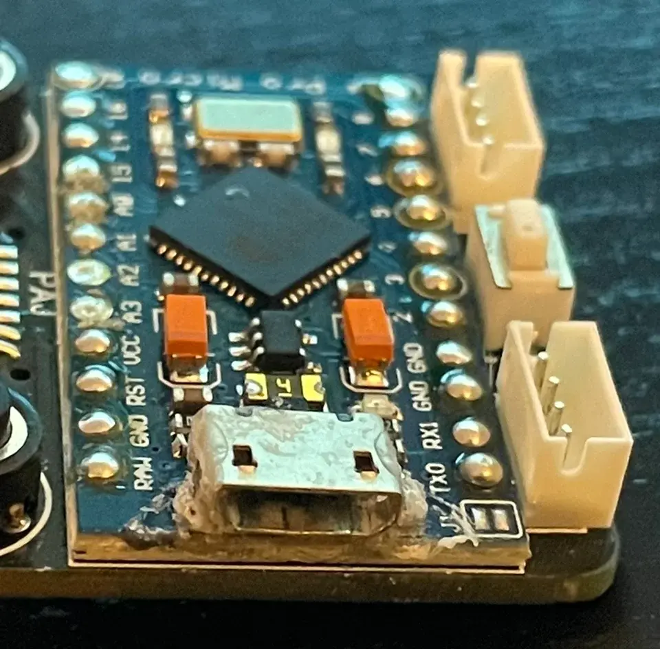 Close-up of a Pro Micro microcontroller board showing a damaged and oxidized Micro USB port with residue.