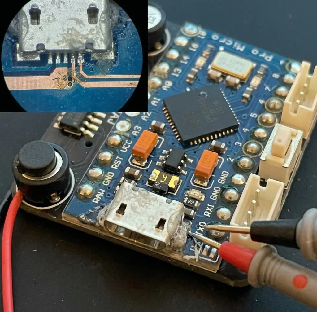 Microscope view and multimeter probes checking broken traces and damaged pads on a Pro Micro USB port.