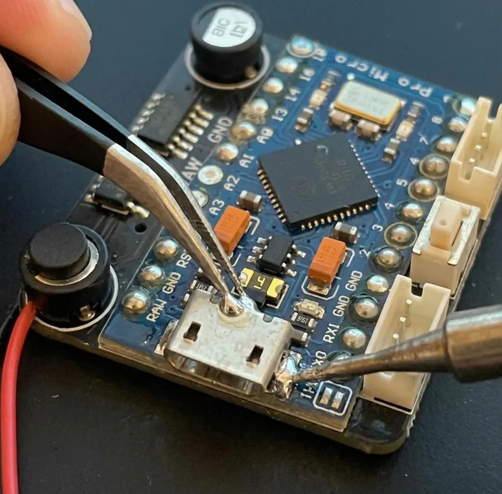 Precision tweezers and micro soldering iron bridging a broken trace on a Pro Micro board.