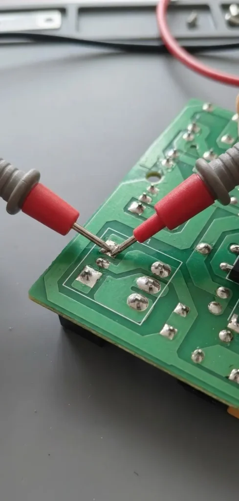 Multimeter probes checking 5V DC coil voltage on PCB solder pads during operation.