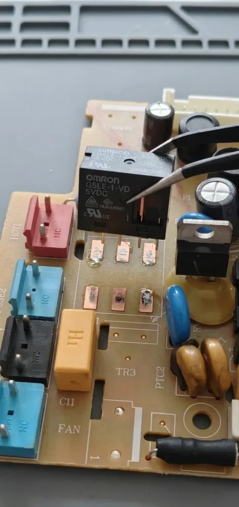 Tweezers positioning an upgraded Omron G5LE-1-VD 5VDC relay over cleaned PCB pads.